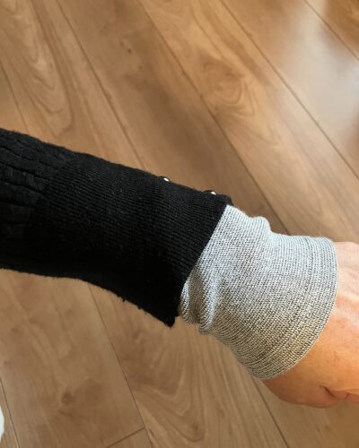 黒のセーターの下にBSファインのアームカバーを着用している腕の写真