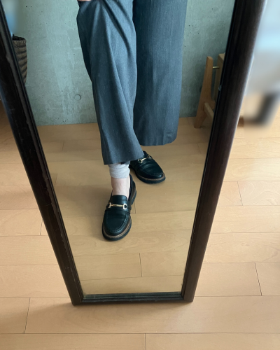 グレーのストレートパンツの下にレッグウォーマーを着用して、素足にローファーを履いた状態で、レッグウォーマーが見えるように足を挙げている写真